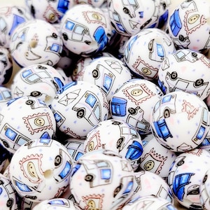May include: A collection of white silicone beads with a blue and pink mail truck pattern. The beads are approximately 1 inch in diameter and have a hole in the center for stringing.