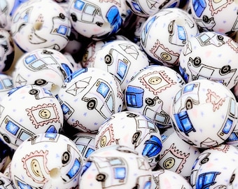 May include: A collection of white silicone beads with a blue and pink mail truck pattern. The beads are approximately 1 inch in diameter and have a hole in the center for stringing.