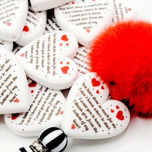 Puede incluir: Una pila de adornos blancos en forma de corazón con corazones rojos y el texto "You have done so much for me. I don't know where to start. I want you to know I thank you, from the bottom of my heart." Los adornos están al lado de un adorno rojo y peludo en forma de corazón.