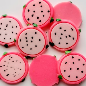 May include: Seven pink and white dragon fruit slices with black seeds. The slices are made of plastic and have a glossy finish.