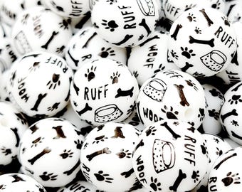 May include: White round beads with black paw prints, dog bones, and food bowls. The word "RUFF" and "WOOF" are printed on the beads. These beads are ideal for crafting projects with a dog theme.