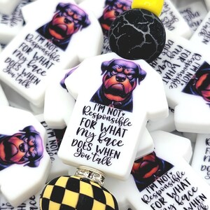 May include: White T-shirt shaped beads with a Rottweiler graphic and the text "I'M NOT RESPONSIBLE FOR WHAT MY FACE DOES WHEN YOU TALK." Also, black and yellow checkered and black crackle beads.