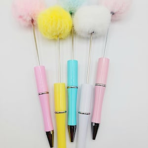 May include: Five colourful ballpoint pens with fluffy pom-poms on top. The pens are pink, yellow, blue, white, and light pink.