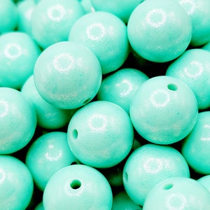 May include: A close-up image of a pile of turquoise blue wooden beads with a shimmery finish. The beads are round and have a hole in the center for stringing.