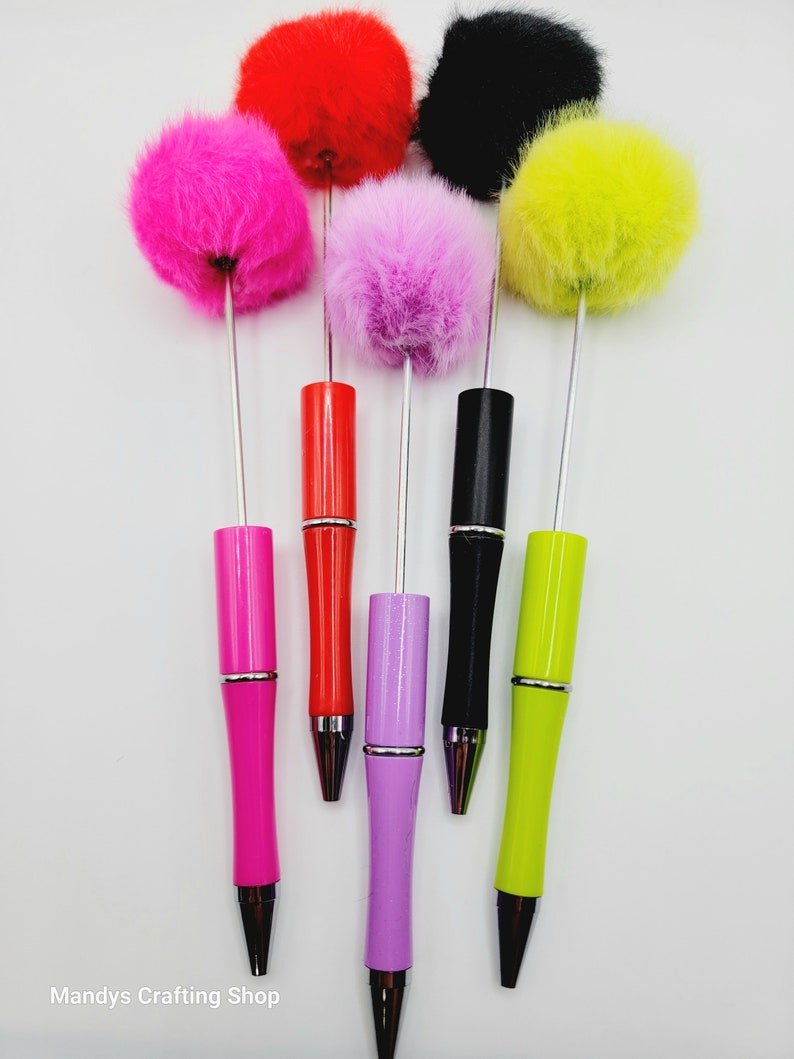May include: Six colourful pens with fluffy pom-poms on top. The pens are pink, red, purple, black, yellow, and green.