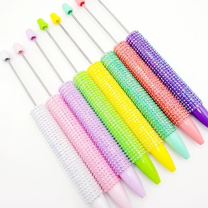 May include: A set of eight colorful pens with a sparkly, iridescent finish. The pens have a silver metal tip and a clear plastic barrel. The colors are white, pink, lavender, light green, yellow, turquoise, coral, and purple.