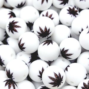 May include: A collection of white, round beads with a cannabis leaf design. The leaves are brown with a leopard print pattern. The beads are smooth and appear to be made of plastic or resin.