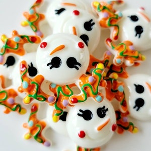 May include: A group of white snowman charms with orange, green, and purple Christmas lights. The charms are made of resin and have a glossy finish.