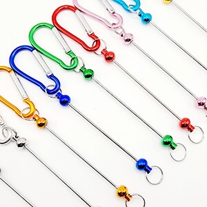 Op de afbeelding: Assortiment van kleurrijke metalen sleutelhangers met een karabijnhaak en een metalen staaf met een bal aan het einde. De sleutelhangers zijn in de kleuren blauw, groen, rood, roze en geel.