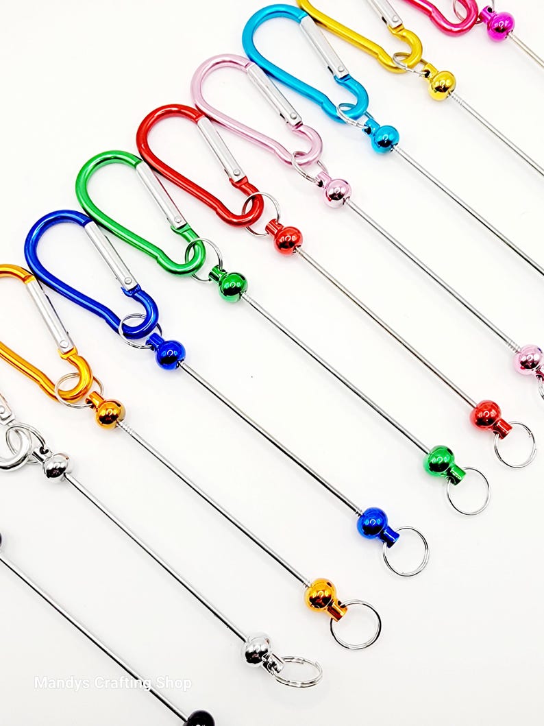 Op de afbeelding: Assortiment van kleurrijke metalen sleutelhangers met een karabijnhaak en een metalen staaf met een bal aan het einde. De sleutelhangers zijn in de kleuren blauw, groen, rood, roze en geel.