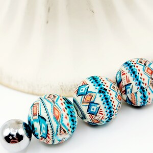 May include: Three round beads with a geometric pattern in shades of blue, orange, and white. The beads are strung on a silver metal connector.