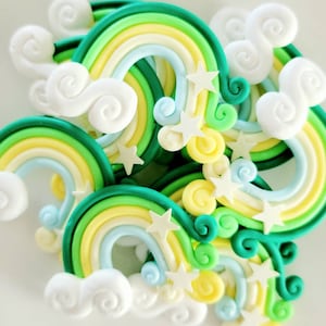 May include: A group of colorful rainbow-shaped decorations with white clouds and stars. The rainbows are made of green, yellow, and blue fondant. The clouds and stars are white.
