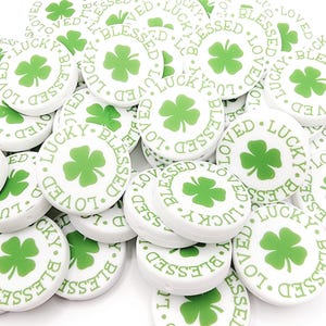 Peut inclure: Un tas de boutons ronds blancs avec un tr&egrave;fle &agrave; quatre feuilles vert et les mots "Lucky", "Blessed" et "Loved" imprim&eacute;s dessus.