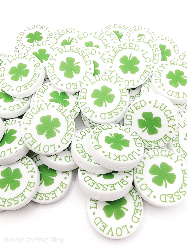 Peut inclure: Un tas de boutons ronds blancs avec un tr&egrave;fle &agrave; quatre feuilles vert et les mots "Lucky", "Blessed" et "Loved" imprim&eacute;s dessus.