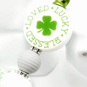 Peut inclure: Stylo blanc et vert avec un charme rond qui dit "Blessed. Loved. Lucky." avec un tr&egrave;fle &agrave; quatre feuilles au centre. Le charme est accentu&eacute; par des strass.