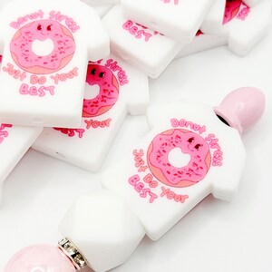 May include: White silicone donut charm with pink frosting and sprinkles. The charm is shaped like a t-shirt with the text "Donut stress, Just Do Your Best" in pink lettering.