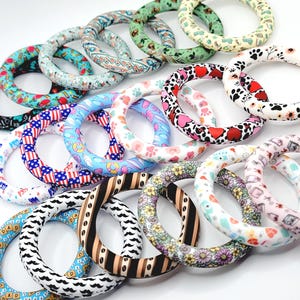 May include: A collection of colorful, patterned silicone teething rings. Designs include paw prints, hearts, floral, mustache, and USA flag patterns. The rings are in various colors, including red, blue, pink, and green. These are designed for babies and toddlers.