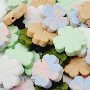 May include: A collection of four-leaf clover shaped silicone beads in various colors, including green, brown, white, pink, and blue. The beads have a hole in the center for stringing.
