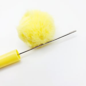 May include: A yellow pom-pom attached to a yellow plastic handle with a thin metal rod extending from the handle.