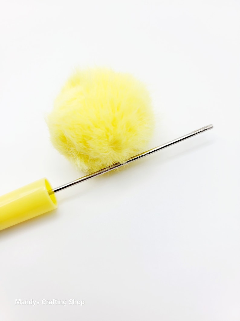 May include: A yellow pom-pom attached to a yellow plastic handle with a thin metal rod extending from the handle.