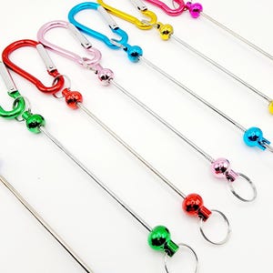 Op de afbeelding: Set van acht kleurrijke metalen sleutelhangers met een karabijnhaak en een metalen bal aan het einde van een lange metalen staaf. De sleutelhangers zijn in de kleuren rood, roze, blauw, groen, geel en paars.
