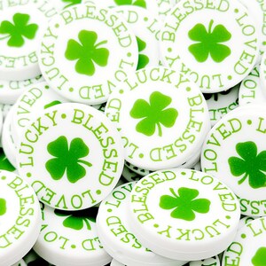 Peut inclure: Un tas de boutons ronds blancs avec des tr&egrave;fles &agrave; quatre feuilles verts et les mots "Lucky", "Blessed" et "Loved" imprim&eacute;s dessus.
