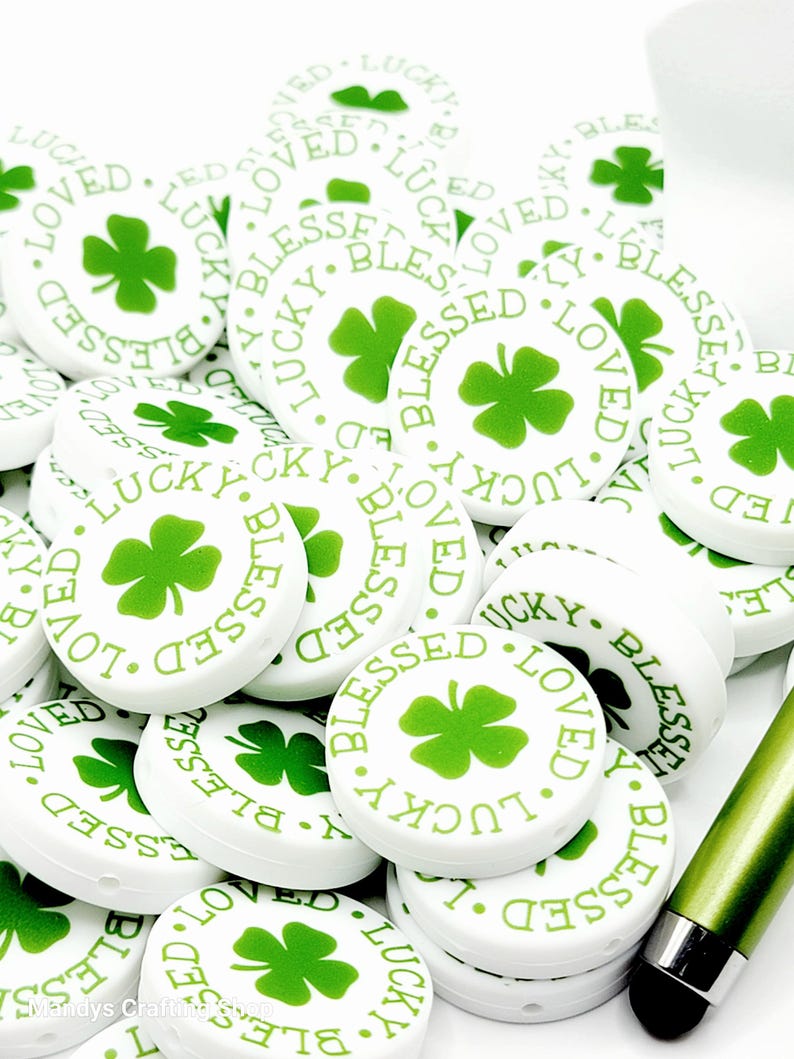 Peut inclure: Un tas de boutons ronds blancs avec un tr&egrave;fle &agrave; quatre feuilles vert et les mots "Blessed", "Lucky" et "Loved" imprim&eacute;s dessus.
