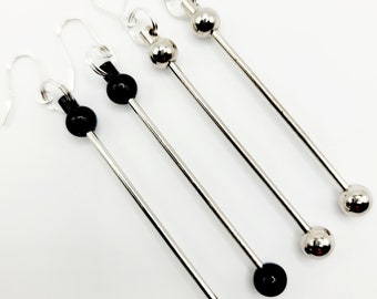 May include: Three pairs of silver dangle earrings with black beads and silver balls at the end. The earrings are long and slender.
