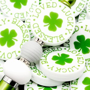 Peut inclure: Gros plan sur un tas de rondins de c&eacute;ramique blancs avec des tr&egrave;fles &agrave; quatre feuilles verts et les mots "Blessed", "Loved" et "Lucky" imprim&eacute;s dessus.