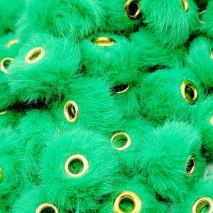 May include: A close-up of a pile of green fuzzy pom-pom beads with gold metal eyelets. The beads are perfect for crafting projects.