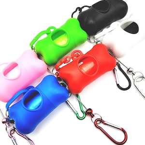 May include: A collection of colorful, bone-shaped dog waste bag dispensers. The dispensers are in various colors, including pink, green, blue, red, black, and white. Each dispenser has a handle and a carabiner clip for easy attachment.
