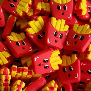 May include: A pile of red and yellow silicone charms shaped like a cartoon french fry container with a smiling face. The charms are for jewelry making or other craft projects.