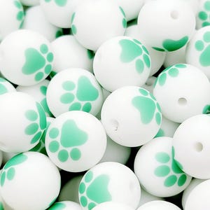 May include: A close-up of a pile of white silicone beads with a green paw print design.