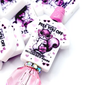 May include: White polymer clay beads with a pink and purple cat graphic wearing sunglasses and the text "PISS YOU OFF". The beads are shaped like a t-shirt and have a pink bead on top. The text "WHAT I DID TO YOU OFF" is also visible.