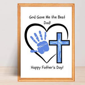 以下が含まれることがあります： 金色のフレームに入った額装されたアートワーク。「God Gave Me the Best Dad!」と「Happy Father's Day!」の文字が特徴です。青い手形が黒いハートの中にあり、青い十字架も描かれています。