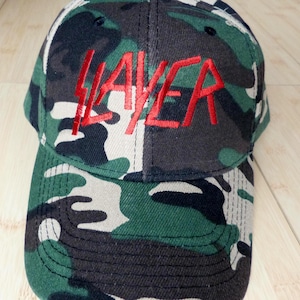 May include: A camouflage baseball cap with the word "SLAYER" embroidered in red on the front.