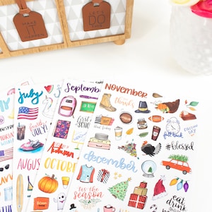 May include: A set of colorful monthly planner stickers featuring illustrations of various themes for each month, including a unicorn for July, a school backpack for September, a turkey for November, and a Christmas tree for December.