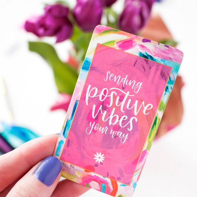 May include: A pink card with a colorful abstract design and gold trim. The card says "Sending positive vibes your way" in white script.