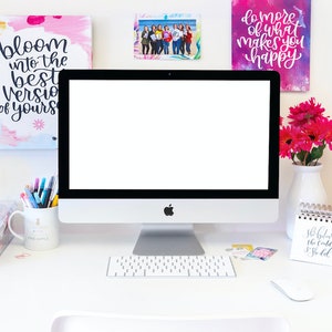 May include: A white desk with a computer, keyboard, mouse, and various office supplies. There are three framed pieces of art on the wall behind the desk. The art features colorful abstract designs and inspirational quotes, including "bloom into the best version of yours" and "do more of what makes you happy".