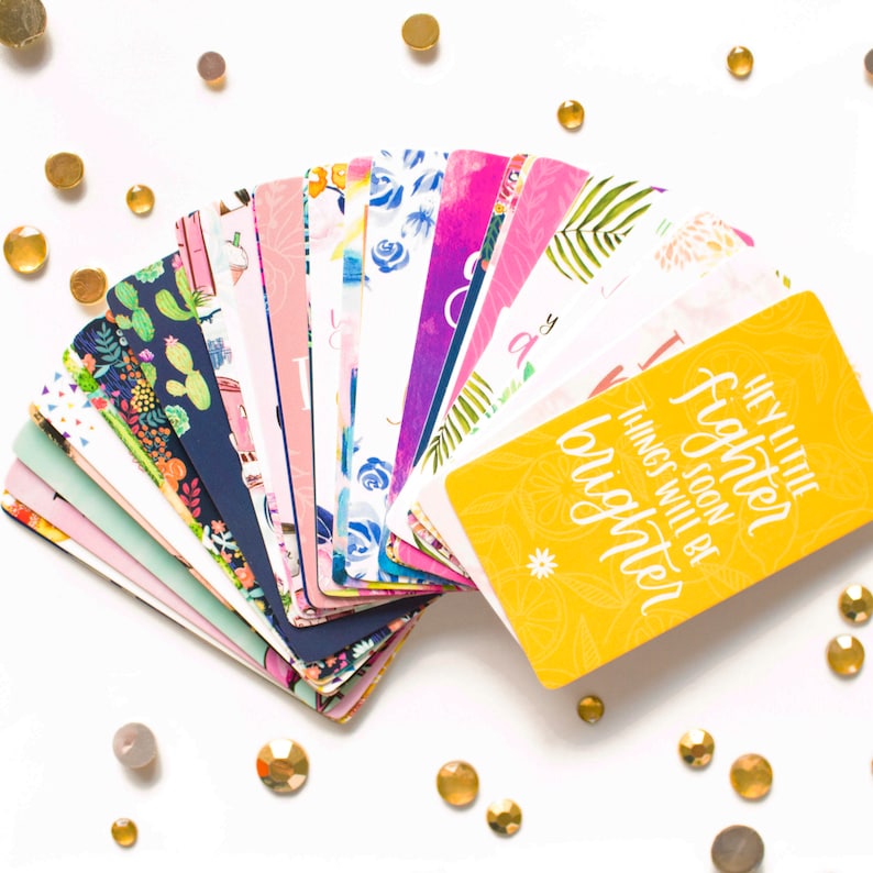 May include: A set of colorful affirmation cards with floral and geometric patterns. The top card is yellow with the text "Hey little fighter, things soon will be brighter."