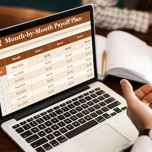 Peut inclure: Un ordinateur portable affiche un tableau "Plan de remboursement mensuel". L'écran présente des données financières avec des colonnes pour "Mois", "Compte 1", "Compte 2" et "Compte 3". L'ordinateur est sur une table en bois, une main se dirigeant vers l'écran.