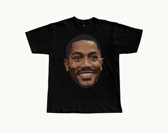May include: A black short-sleeve t-shirt featuring a large, centered, realistic photographic print of a smiling man with short dark hair and a mustache. The graphic is positioned on the chest area of the garment, which has a standard crew neckline.