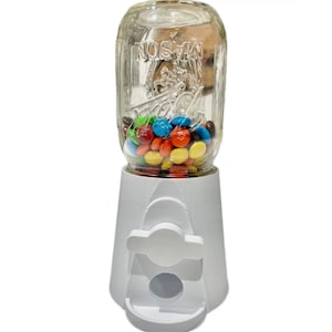 May include: A white candy dispenser with a clear glass jar filled with colorful M&Ms. The jar has the text "MASON" printed on it.