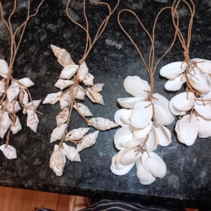 Può includere: Quattro ornamenti di conchiglie fatti a mano con spago marrone appeso in alto. Ogni ornamento è fatto di diversi tipi di conchiglie, alcune sono bianche e alcune sono marroni.