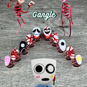 May include: An artistic arrangement featuring nail art with various face designs and a central mask figure. The word "Gangle" is displayed in green. The nails showcase a range of colors and patterns, including red, white, and black.