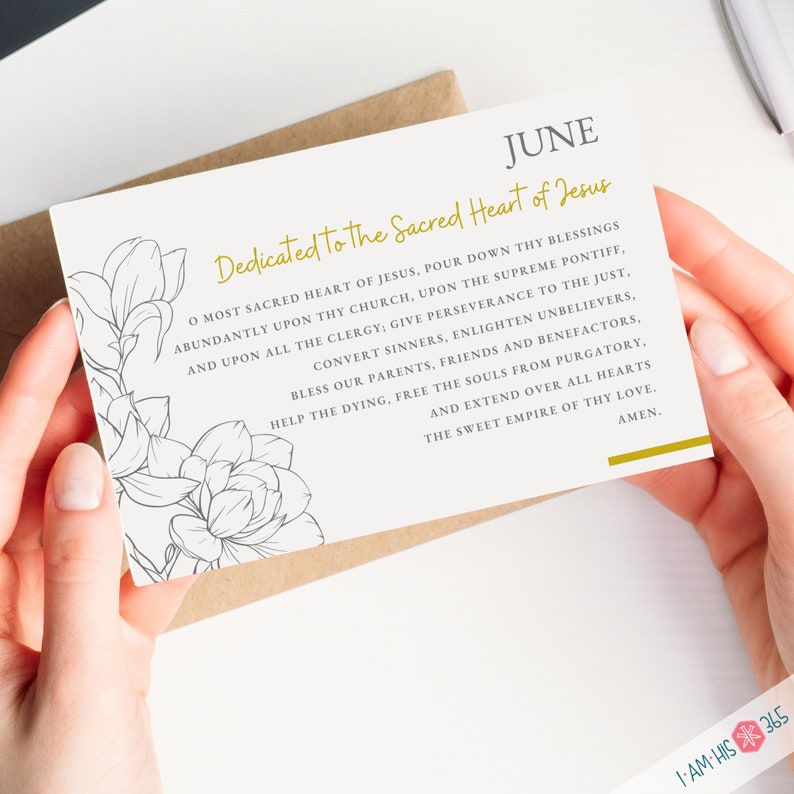 May include: A white card with gold lettering that reads "JUNE Dedicated to the Sacred Heart of Jesus". The card features a floral design with a black and white outline.