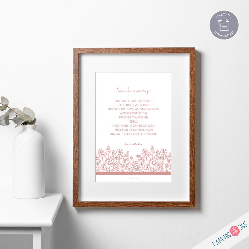 May include: A printable wall art print with a white background and pink text. The text reads "hail mary" and includes the Hail Mary prayer. The text is surrounded by a border of pink flowers.