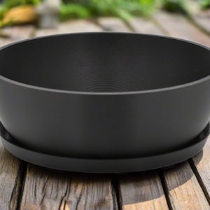 May include: A black plastic planter with a matching saucer. The planter is round and has a smooth, slightly textured surface.