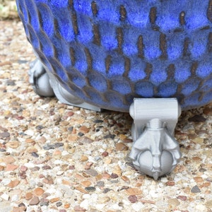 May include: A blue ceramic planter with a textured surface and three gray, claw-like feet.
