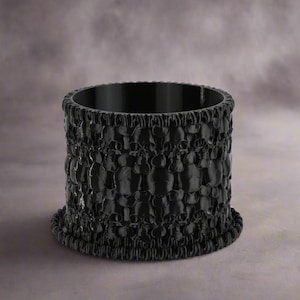 May include: Black napkin ring with a textured design of small circles. The ring is made of a smooth, hard material.